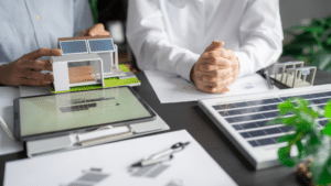 Maquette d’un bâtiment tertiaire avec panneaux photovoltaïques, tablette et documents techniques sur la gestion énergétique et le stockage solaire.