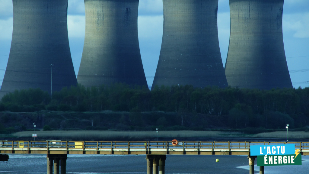 Quatre imposantes tours de refroidissement d’une centrale énergétique dominent l’arrière-plan, symboles d’une production électrique centralisée. Au premier plan, une passerelle surplombe une étendue d’eau paisible, contrastant avec l’infrastructure industrielle. Cette scène illustre les tensions et équilibres entre besoins énergétiques, territoires et mutations du mix énergétique.