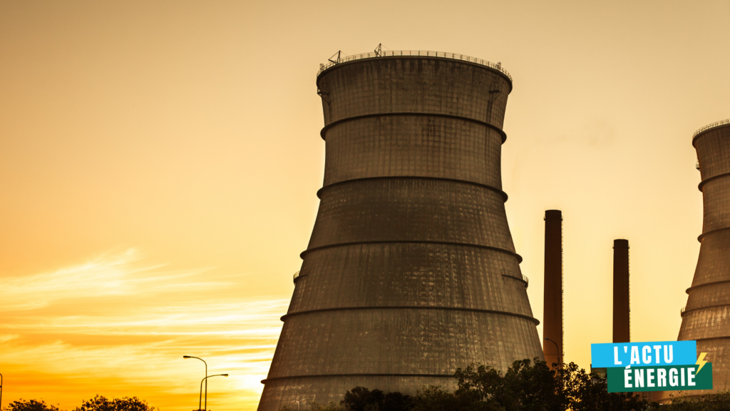 Tours de refroidissement d'une centrale électrique au coucher du soleil, avec le ciel orangé en arrière-plan et des cheminées visibles à droite.
