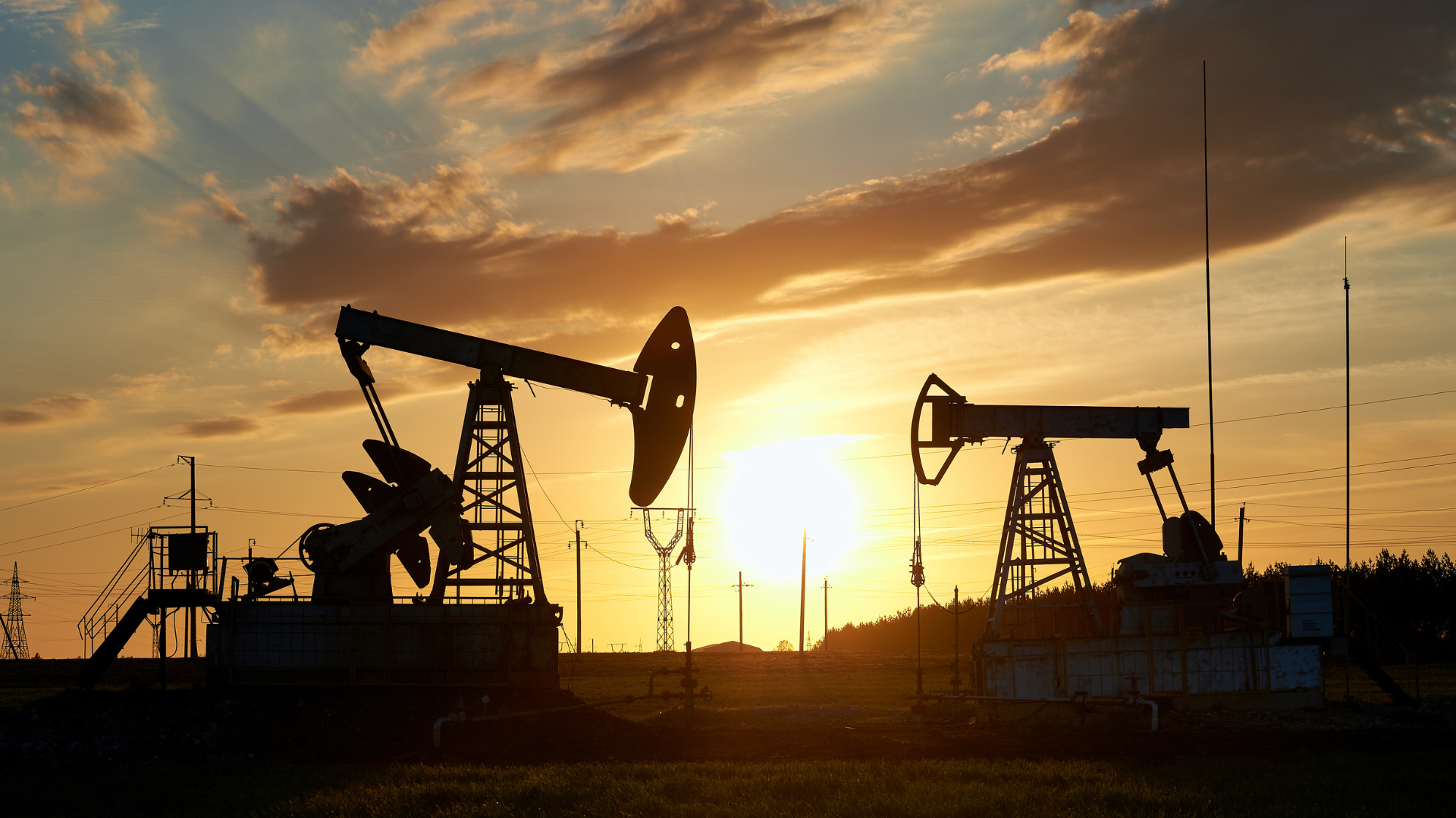 Pompes à balancier d'extraction pétrolière au coucher du soleil, lignes électriques en arrière-plan